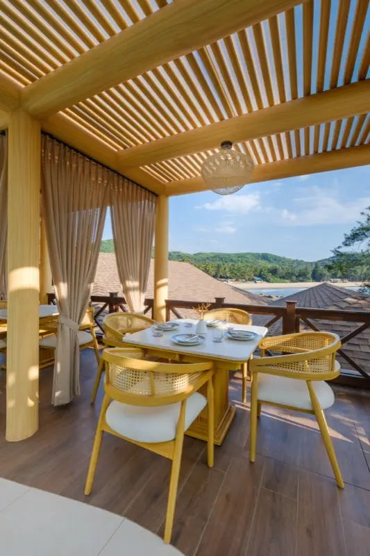 Dining table under wooden pergola overlooking beach and hills