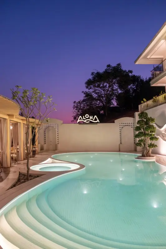 Pool illuminated at twilight with Aloha neon sign and purple sky
