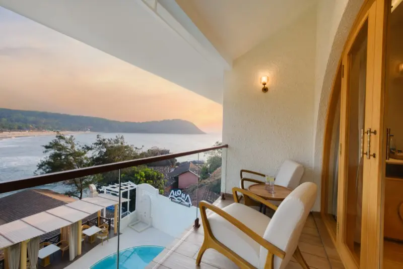 Room 203 balcony with chairs overlooking pool and sea at sunset